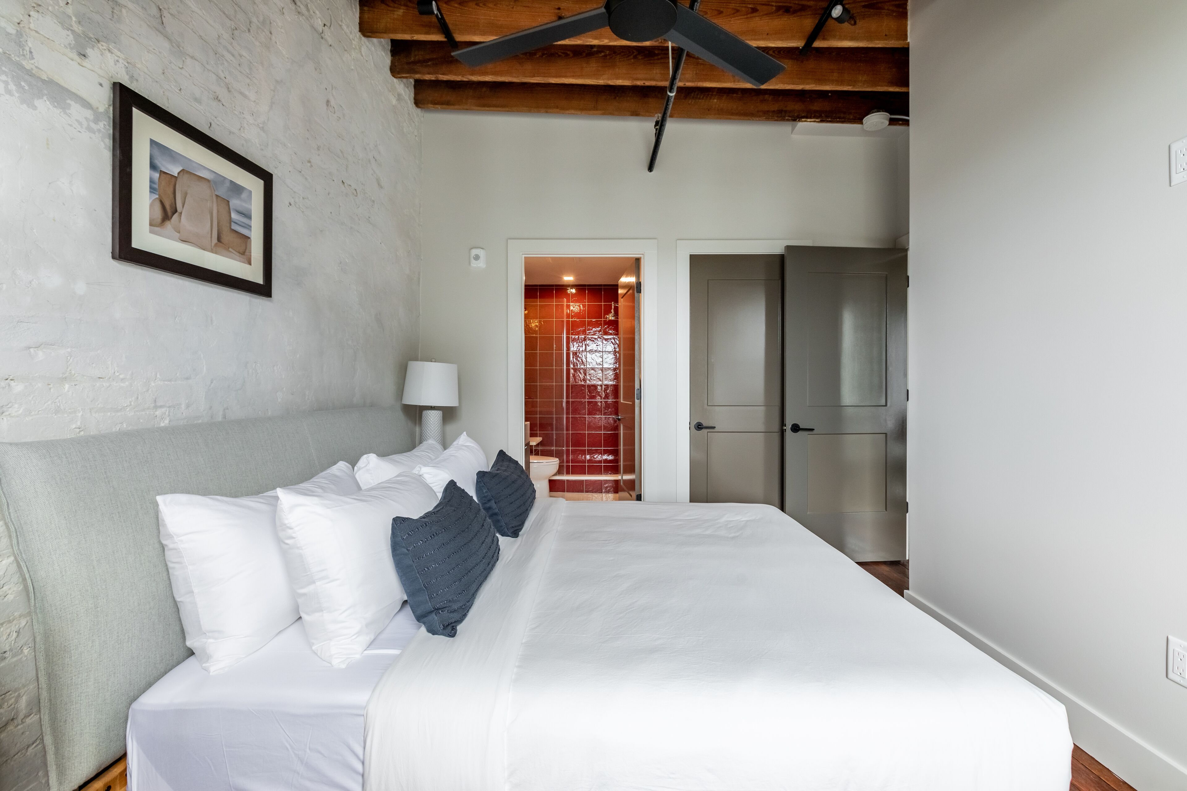 A bedroom with a large bed, a wooden ceiling fan, and a white brick wall.