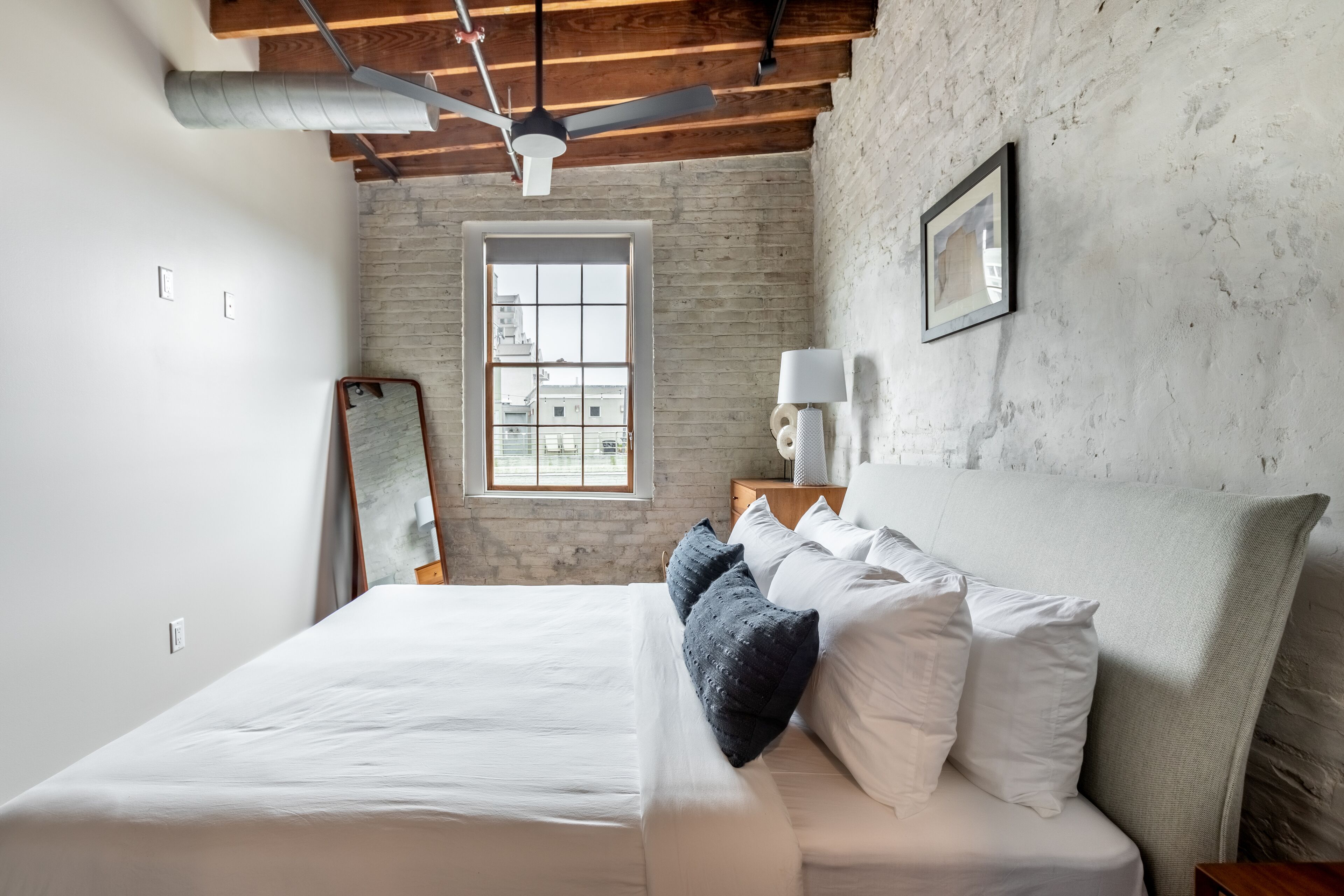 A bedroom with a large bed, a ceiling fan, a window with a view, and a wooden headboard.