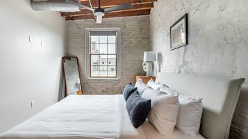 A bedroom with a large bed, a ceiling fan, a window with a view, and a wooden headboard.