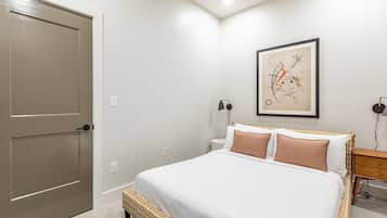A bedroom with a large bed, a wooden bench, a wall-mounted artwork, and a bedside table with a lamp.