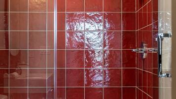 Un bagno moderno con pareti rivestite in piastrelle rosse, una cabina doccia in vetro e un lavandino bianco.