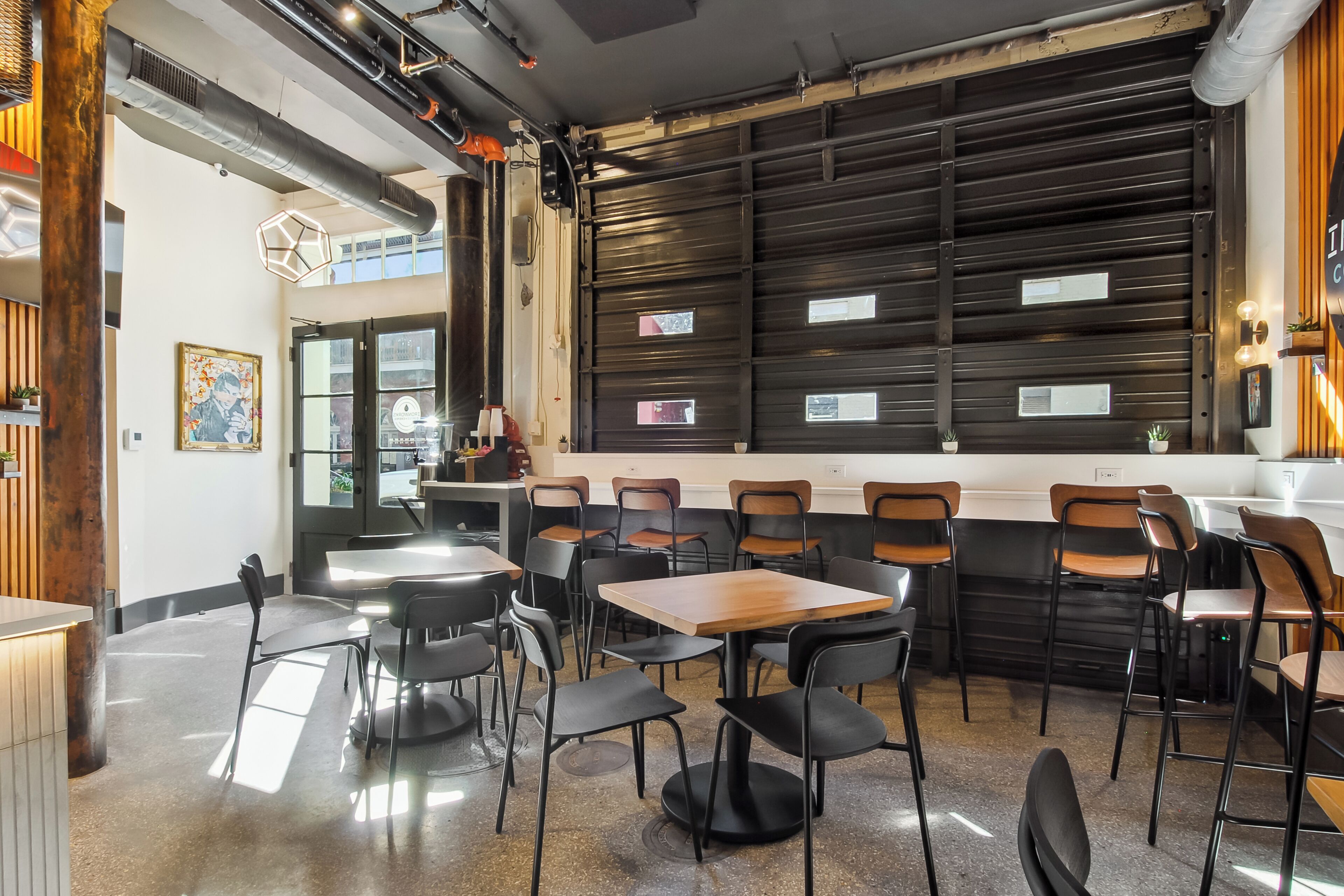 A modern cafe interior with black and wooden chairs, a counter with a menu, and a large window.