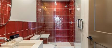 A modern bathroom with a glass shower enclosure, a white toilet, and a vanity with a towel rack.