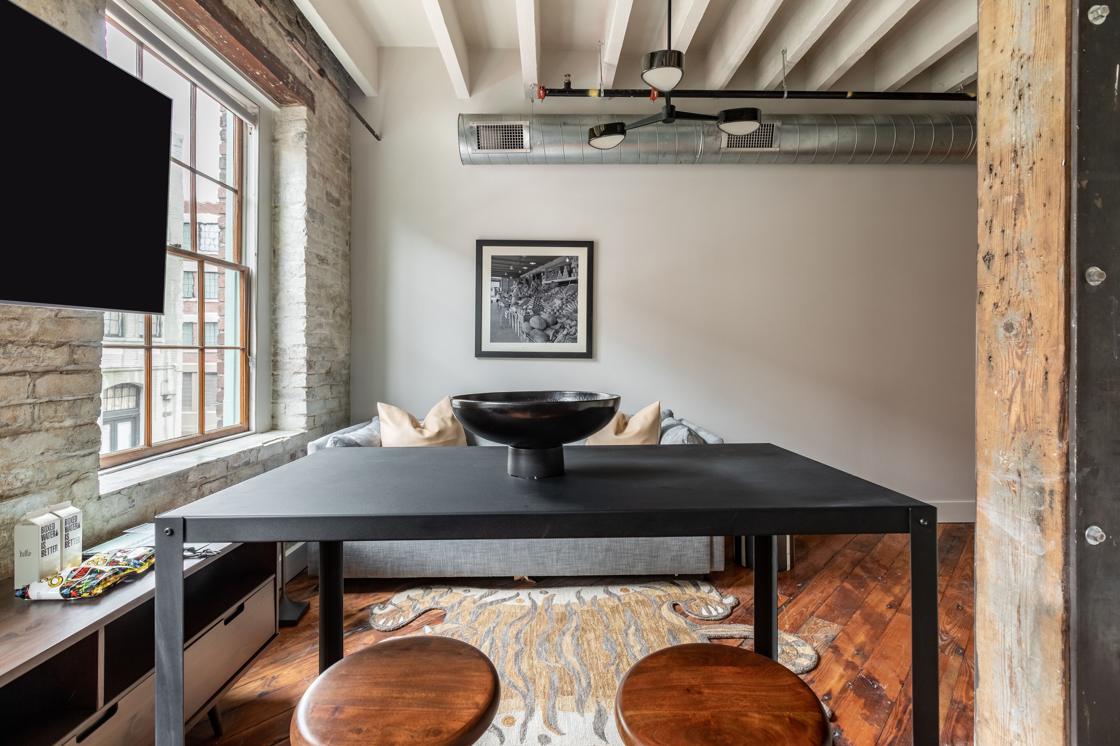 Una cocina moderna con una mesa negra, taburetes de madera, un ventanal grande y una fotografía blanco y negro en la pared.