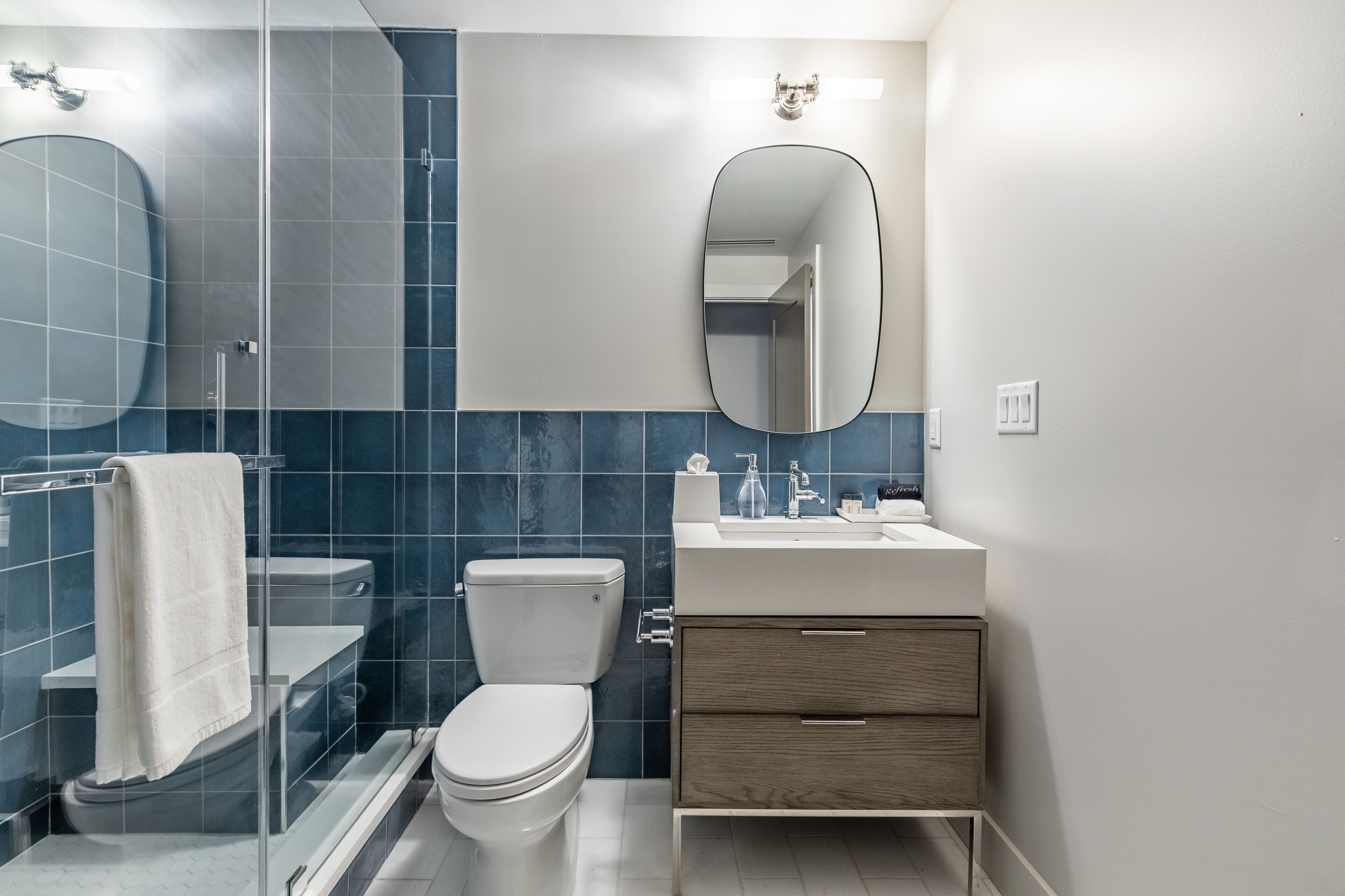 Une salle de bain moderne avec une douche à parois de verre, des toilettes, un lavabo avec un miroir et un meuble-lavabo avec des tiroirs.