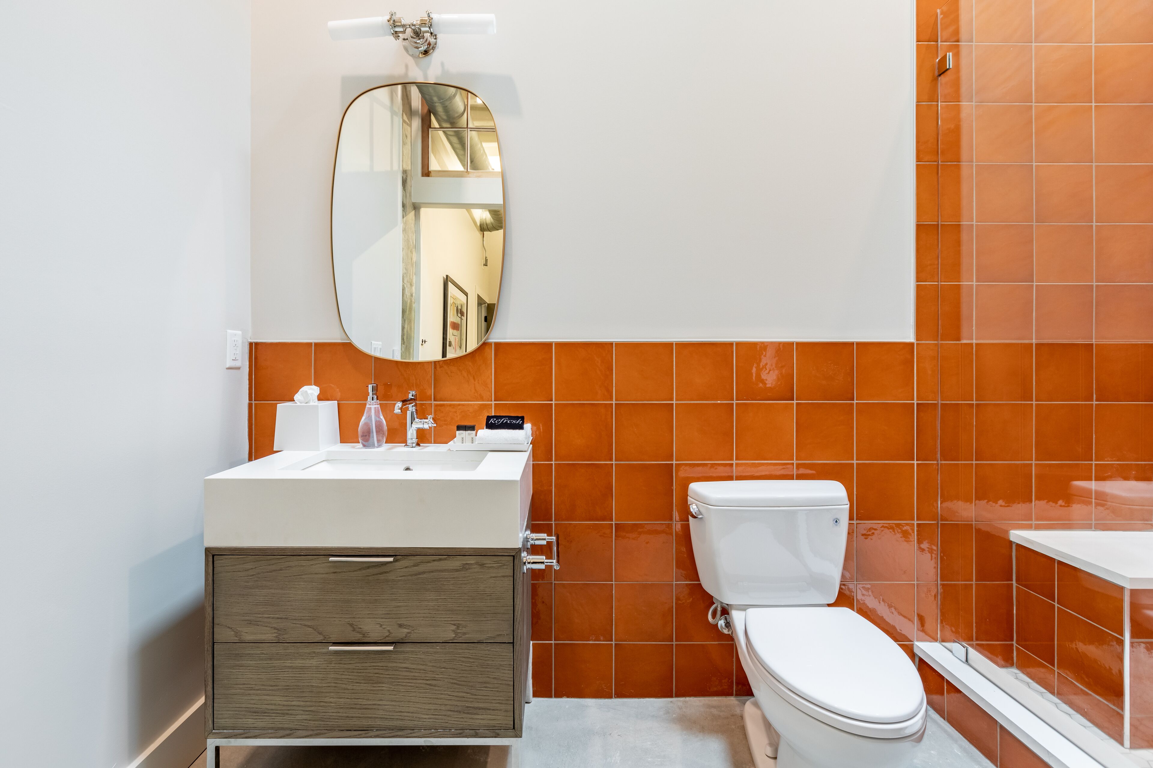 A bathroom with a white sink, a mirror, a toilet, and orange-tiled walls.