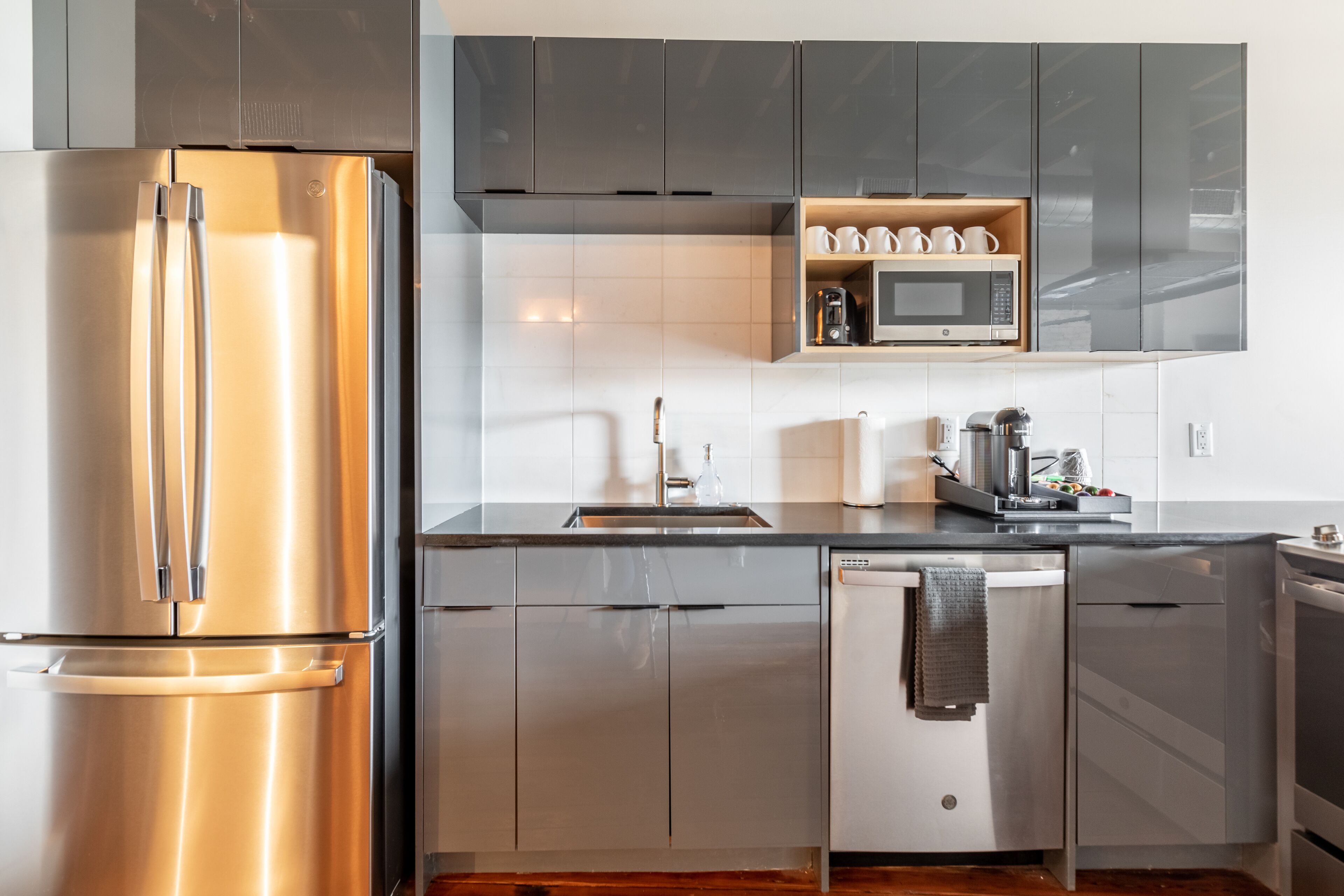 Una cucina moderna con elettrodomestici in acciaio inossidabile, mobili grigi e ripiano integrato per il microonde.