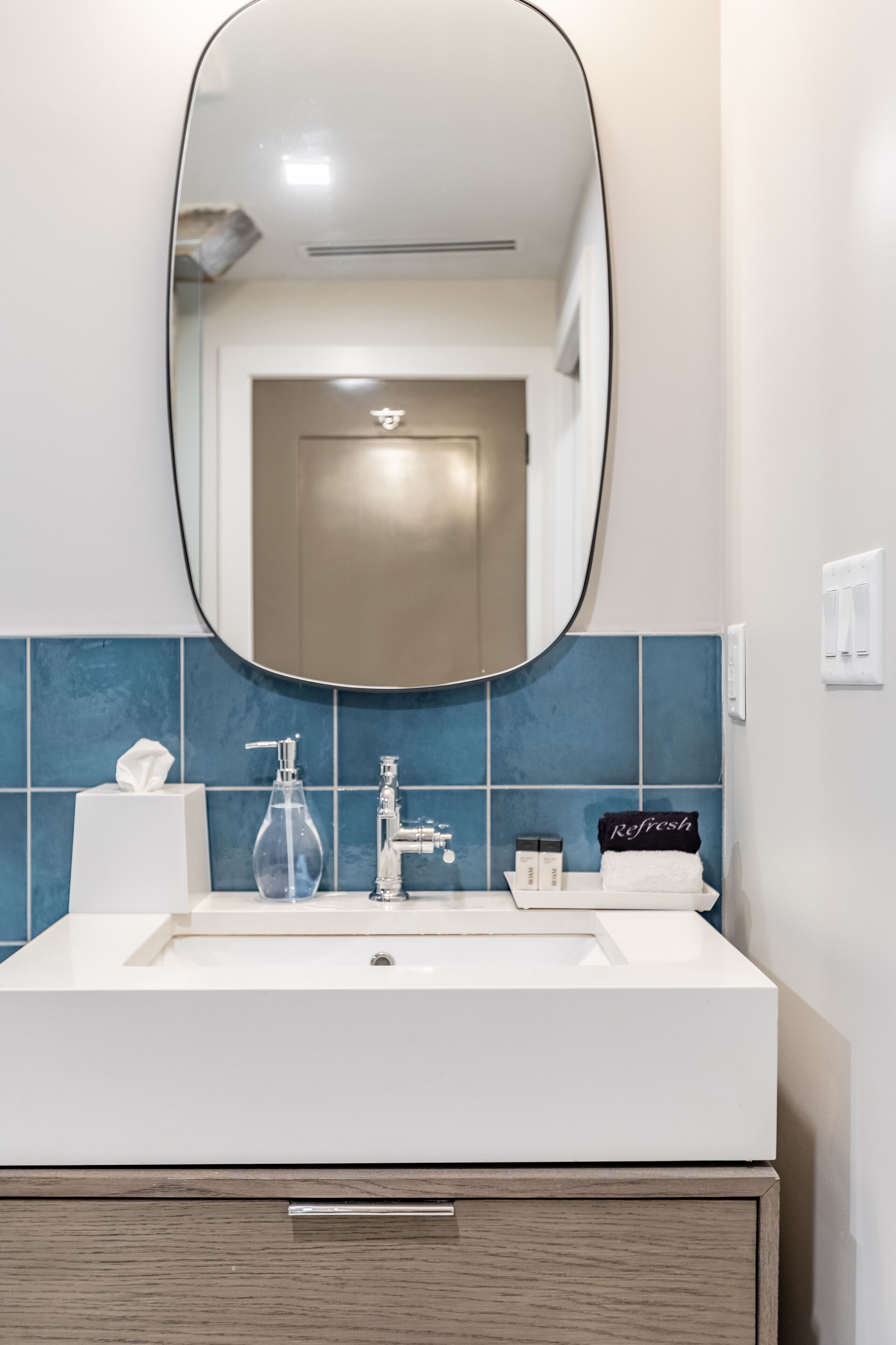 A bathroom with a white sink, a mirror, and blue tiles.