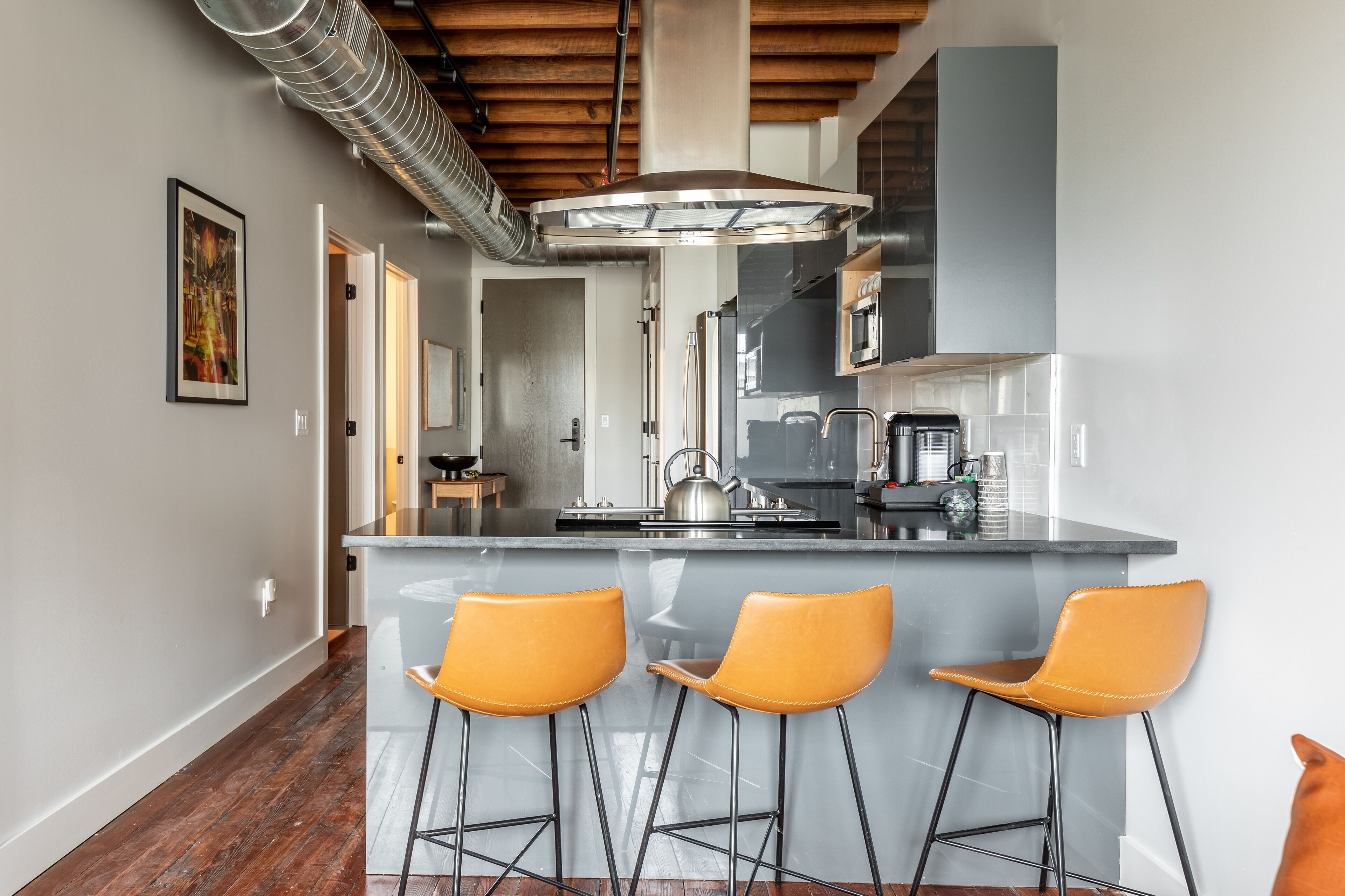 A modern kitchen with a central island, bar stools, stainless steel appliances, and a visible duct system.