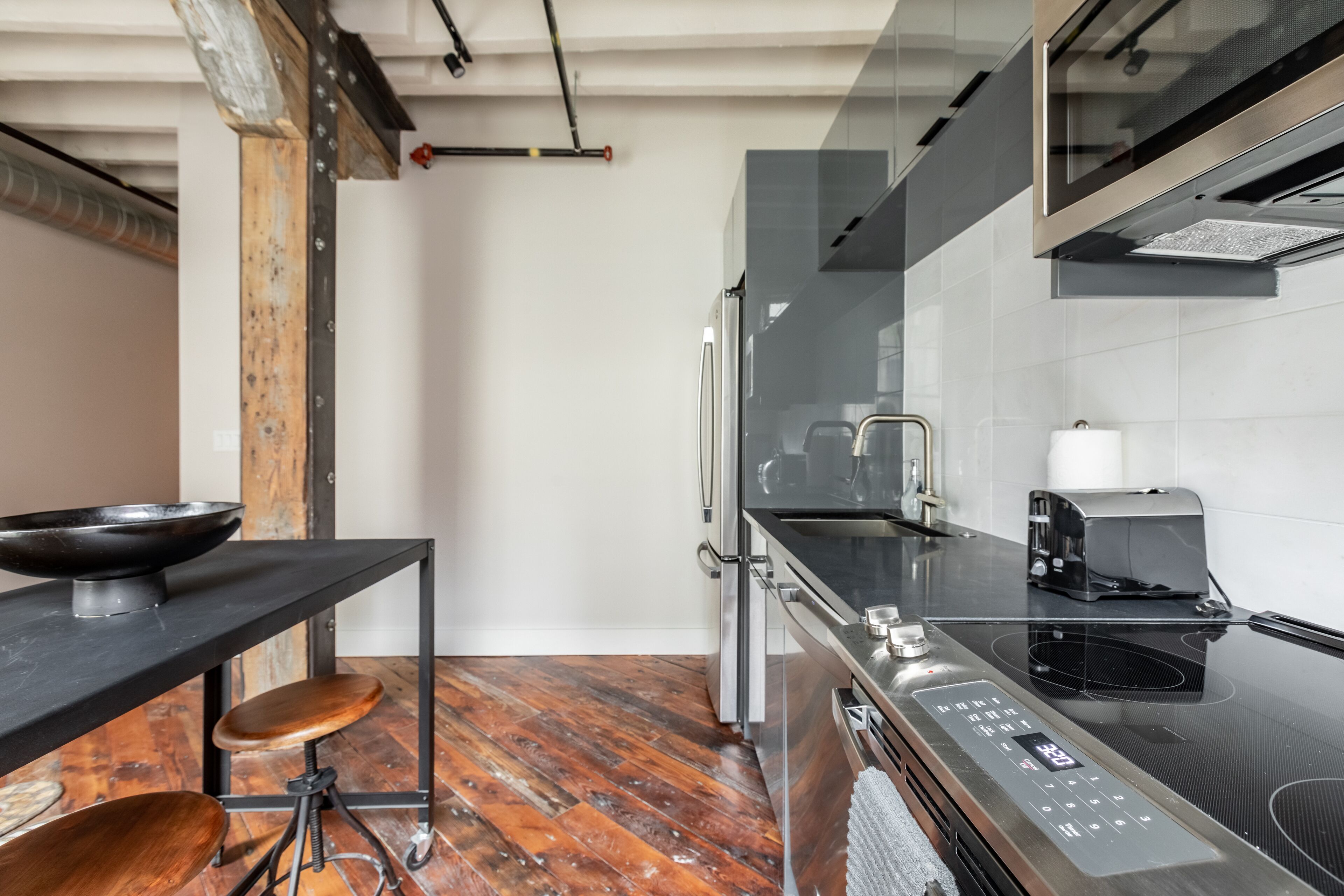 A modern kitchen with a black countertop, stainless steel appliances, and a wooden stool.