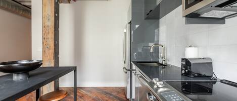 Una cocina moderna con encimera negra, electrodomésticos de acero inoxidable y un taburete de madera.