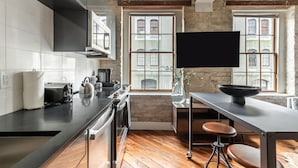 A modern kitchen with a large window, wooden flooring, and a black countertop. - Ironworks (New Orleans)