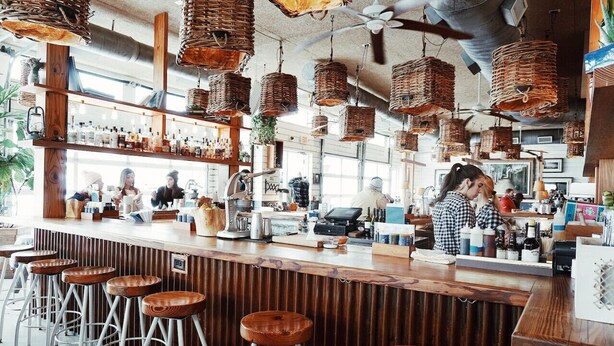 A bar area with wooden stools, a counter, and hanging wicker baskets.