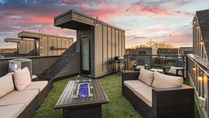A rooftop patio with outdoor furniture, a barbecue grill, and string lights.