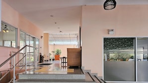 A hotel lobby with a staircase leading to the upper floor, a reception desk, and a large window with a view of the outside. - Nanthana Villa (Pattaya)