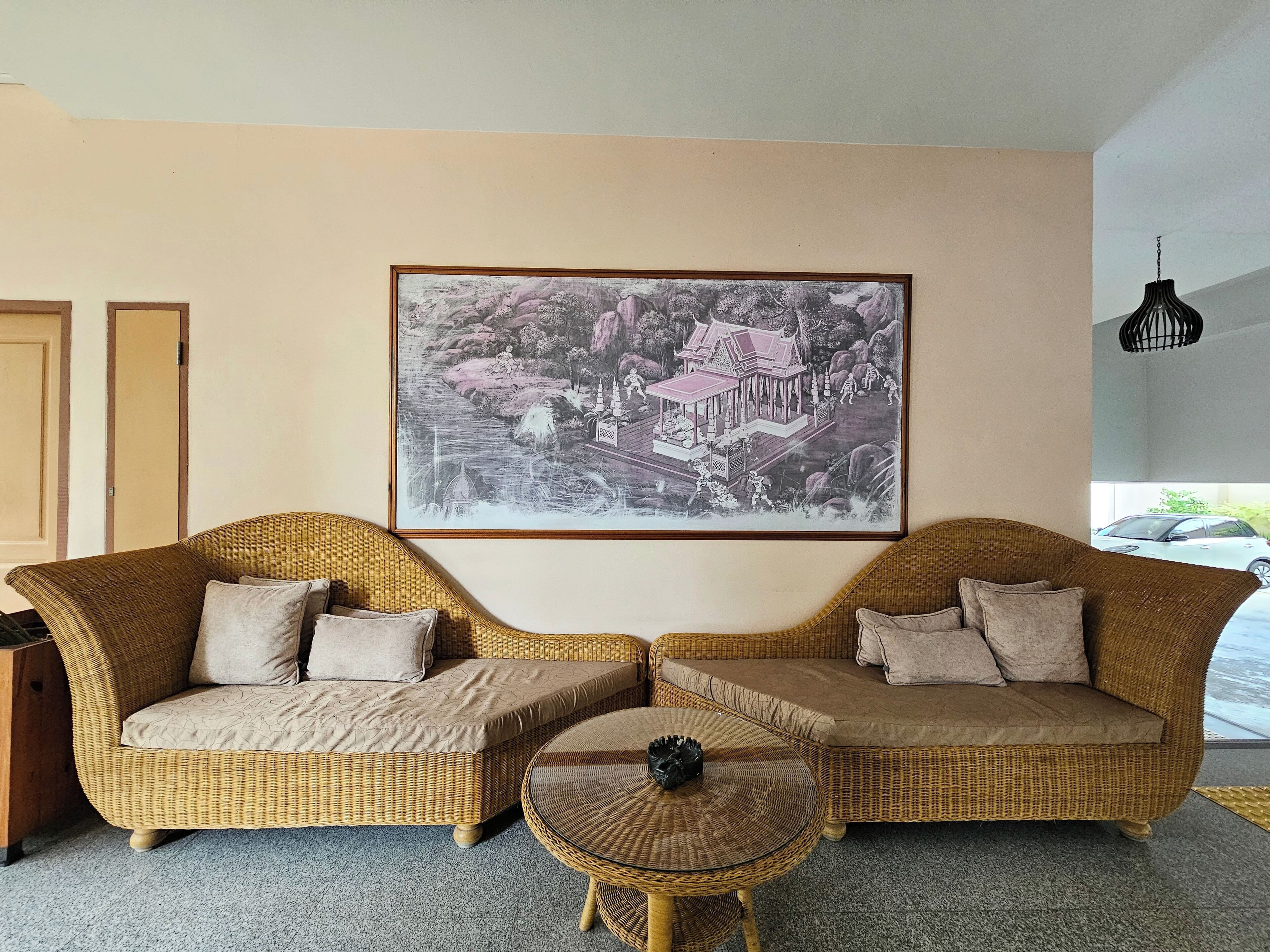 A room with two wicker sofas, a small round table, and a large framed picture on the wall.