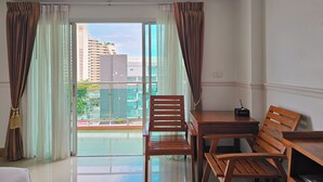 A hotel room with a balcony, wooden furniture, and a view of buildings and greenery. - Nanthana Villa (Pattaya)
