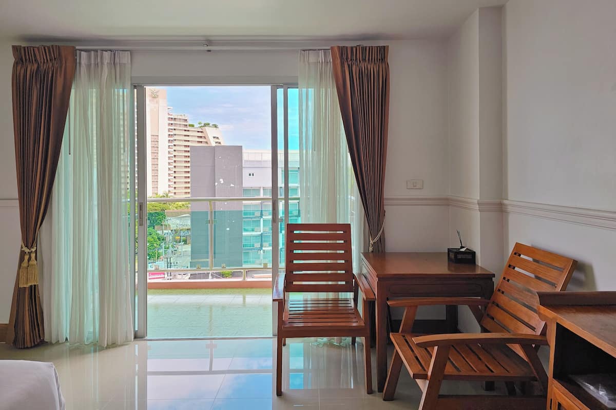 A hotel room with a balcony, wooden furniture, and a view of buildings and greenery.