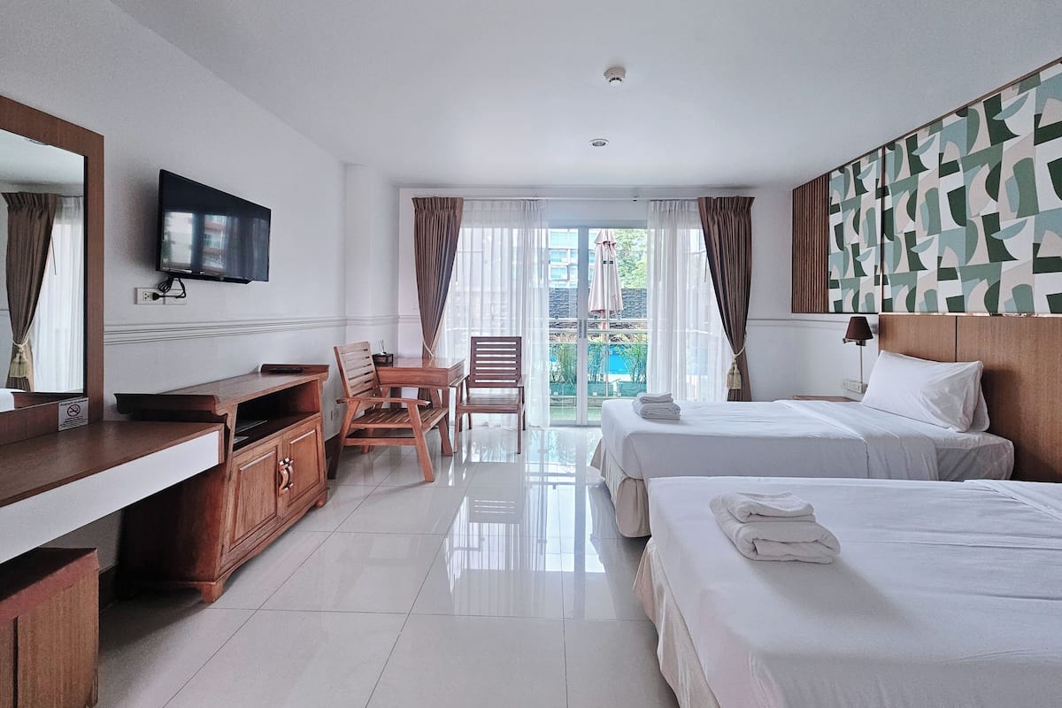A hotel room with a TV, wooden furniture, a balcony with curtains, and a patterned wall.
