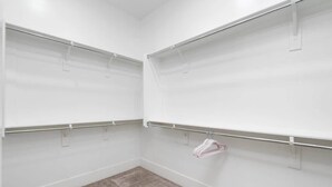 Ein begehbarer Kleiderschrank mit offenen Regalen und einer Kleiderstange, mit einem hellen Teppichboden.