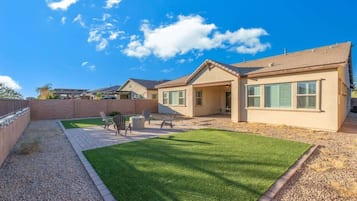 A residential property with a well-maintained lawn, patio furniture, and a clear blue sky.