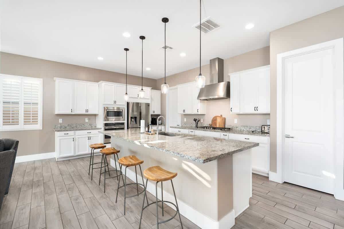 A modern kitchen with white cabinetry, a central island with stools, stainless steel appliances, and pendant lighting.