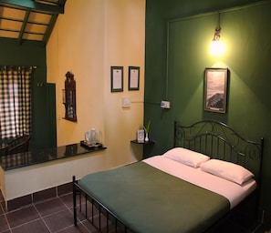 A bedroom with a bed, a nightstand, a mirror, a window with curtains, and a wall-mounted light. - The Last Shola Cottages (Yercaud)