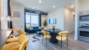 Una sala de estar moderna con un sofá, sillas amarillas, una mesa de comedor y una cocina con estufa.