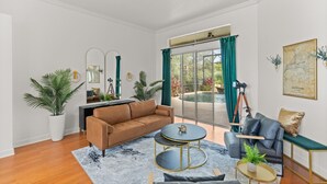 Una sala de estar moderna con un sofá marrón, una mesa de centro redonda y un sofá gris. Hay un ventanal con cortinas, una planta en maceta y un cuadro en la pared.