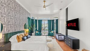Un dormitorio moderno con cama, televisor, ventilador de techo y vistas al exterior.
