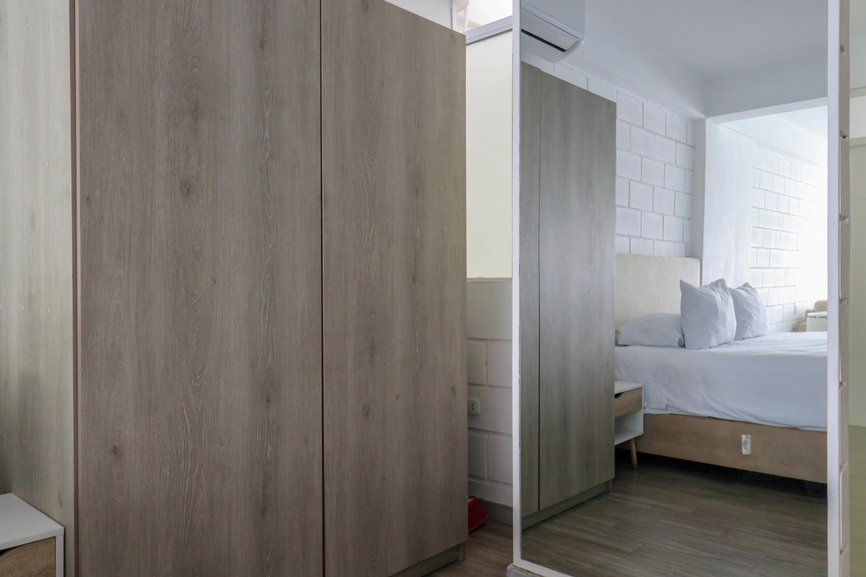 Quarto com guarda-roupa de madeira, cama com roupa de cama branca e parede de tijolos brancos.