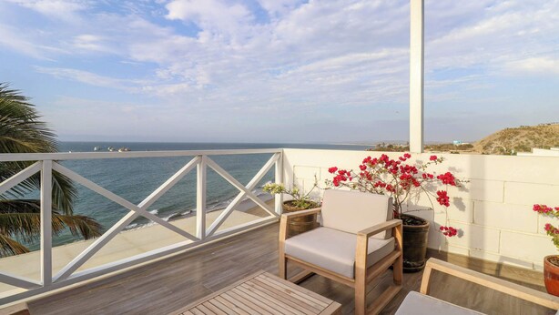 A balcony with a view of the sea, a wooden table, a chair, and potted plants.