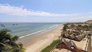 A beach resort with thatched-roof huts, a sandy beach, and boats in the water.
