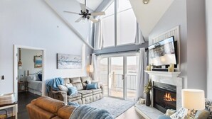 Een ruime woonkamer met een open haard, een plafondventilator en een groot raam met uitzicht op een balkon.