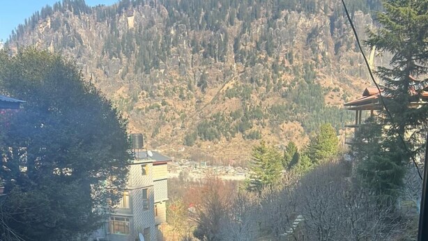 Une vue depuis un balcon donnant sur une région montagneuse, avec un bâtiment visible au loin.