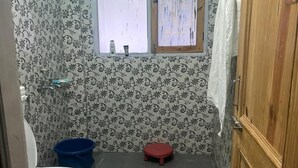 Une petite salle de bain avec des toilettes, un seau bleu et un tabouret rouge.