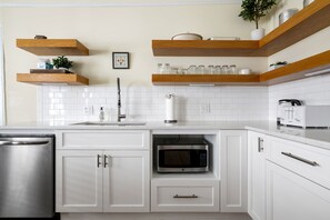 A modern kitchen with white cabinets, a stainless steel dishwasher, a microwave, and wooden shelves above the countertop.