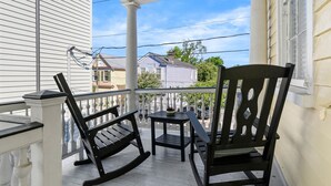 A porch with white columns, black rocking chairs, and a small table with a bowl. - Edisto & Cooper House | Sleeps 14 | Full House (Charleston)