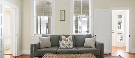 A living room with a gray sofa, patterned cushions, and a woven rug.