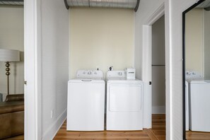 A laundry room with two white front-loading washers and dryers, a brown leather couch, and a white lamp.