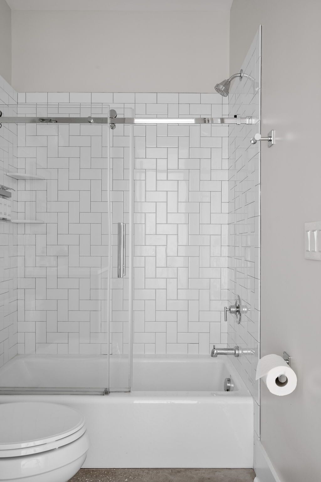 A bathroom with a shower, toilet, and a toilet paper holder.