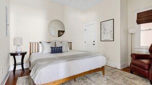 A bedroom with a bed, a round mirror, a framed map, a brown leather chair, and a patterned rug. - Downtown Historic Condo Steps to King St (Charleston)