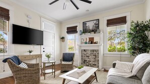 A living room with a television, wicker furniture, a fireplace, and large windows. - Downtown Historic Condo Steps to King St (Charleston)