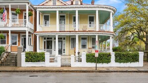 A two-story house with a wrap-around porch, a front entrance, and a small front yard with a hedge. - Downtown Historic Condo Steps to King St (Charleston)