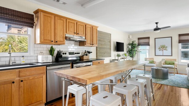A modern kitchen with wooden cabinets, a central island with stools, stainless steel appliances, and a view of the outdoors. - Historic Condo Just Steps to Upper King Street (Charleston)