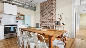 Una cocina moderna con chimenea de ladrillo, muebles blancos y una mesa de comedor de madera con sillas blancas.