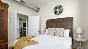 Un dormitorio con una cama grande, cabecera de madera, dos mesitas de noche con lámparas, un armario de madera y una corona decorativa en la pared.