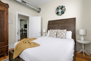 A bedroom with a large bed, a wooden headboard, two bedside tables with lamps, a wooden wardrobe, and a decorative wreath on the wall. - Edisto House | Great for Group Stays | Nightlife (Charleston)