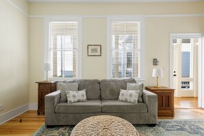 A living room with a gray sofa, patterned cushions, a woven ottoman, and a blue patterned rug. - Edisto House | Great for Group Stays | Nightlife (Charleston)