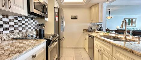 Una cocina moderna con microondas, horno y electrodomésticos de acero inoxidable. Cuenta con ventilador de techo e iluminación empotrada. La cocina tiene un salpicadero de azulejos y encimera de granito.